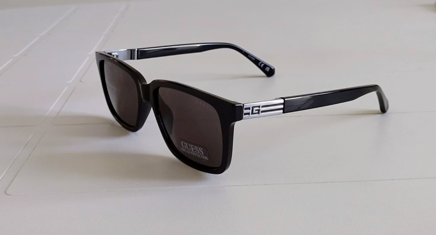 Black sunglasses with a brand logo on a light gray surface