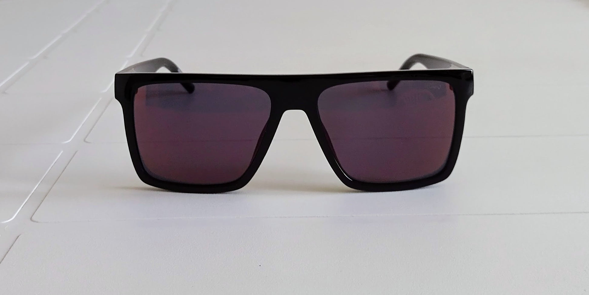 Black sunglasses with purple lenses on a white surface