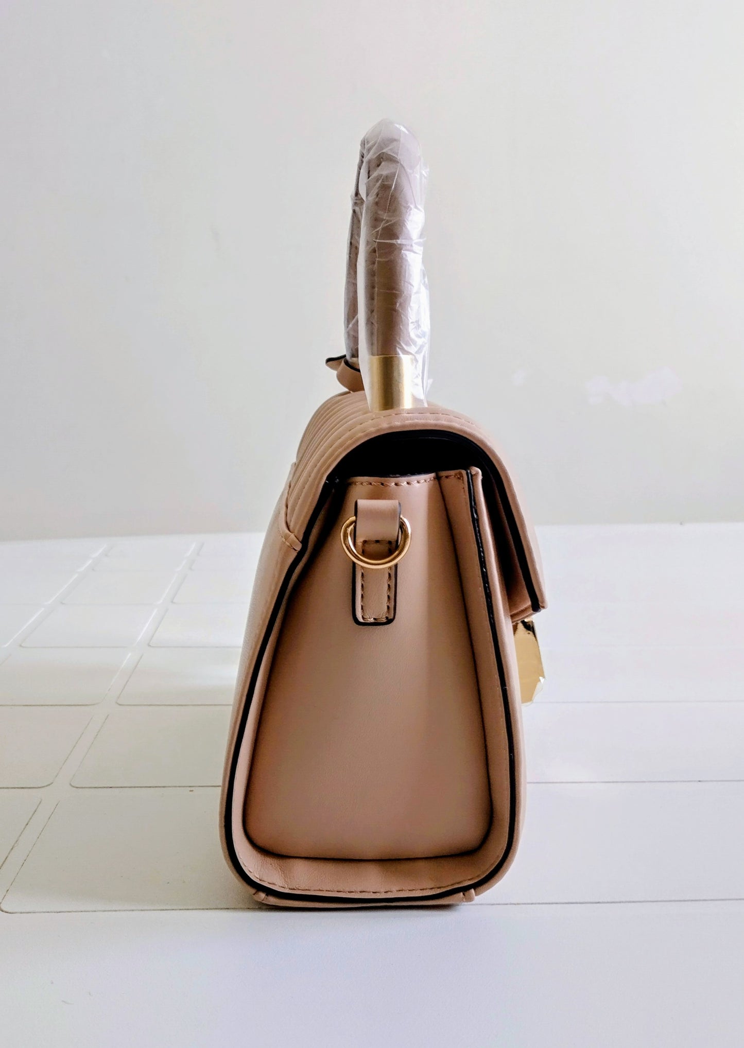 Beige handbag with a gold handle on a white surface