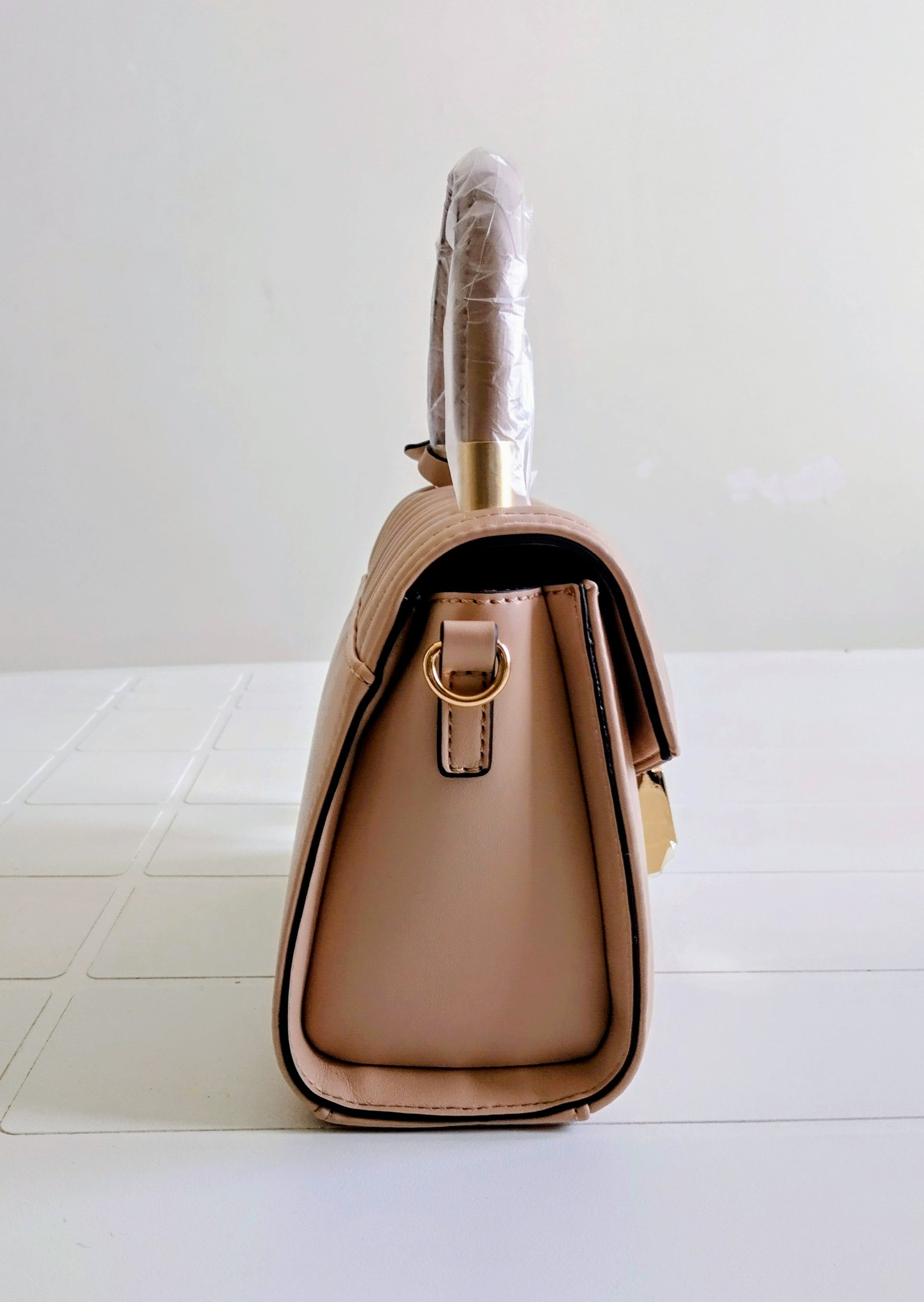 Beige handbag with a gold handle on a white surface
